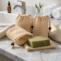 Three natural beige mesh drawstring soap bags with wooden beads, shown with a green bar of soap on a white background.